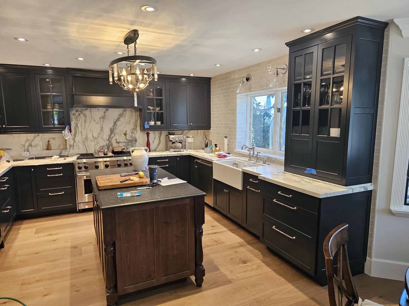 Black cabinet kitchen remodel with marble slab backsplash, farmhouse sink, and glass-front display cabinetry