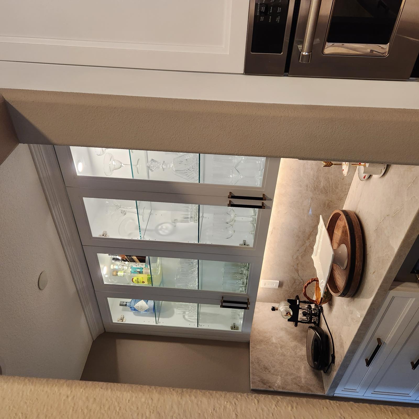 Butler's pantry with lit glass-front cabinets, stone slab backsplash, and quartz counter