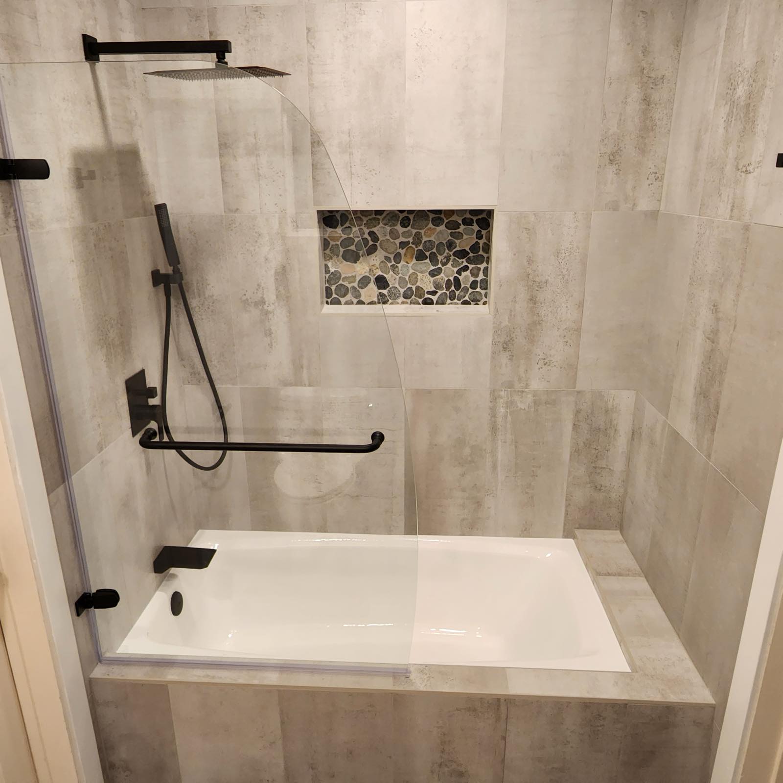 Concrete-look large format tile tub and shower with pebble mosaic niche and matte black fixtures
