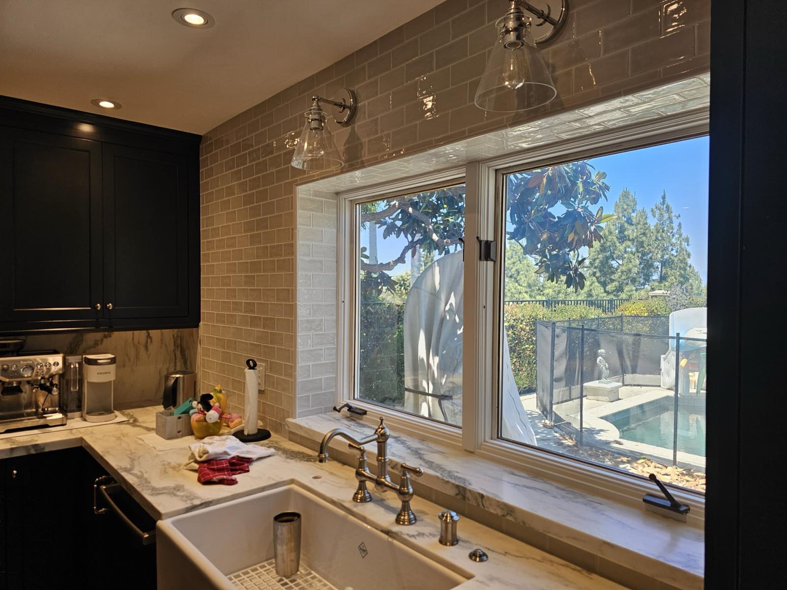 Kitchen sink window with farmhouse apron sink, marble countertops, and glazed subway tile backsplash