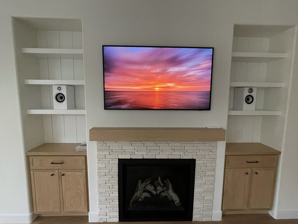 Living room media wall with white brick fireplace, wood mantel, mounted TV, and built-in shelving