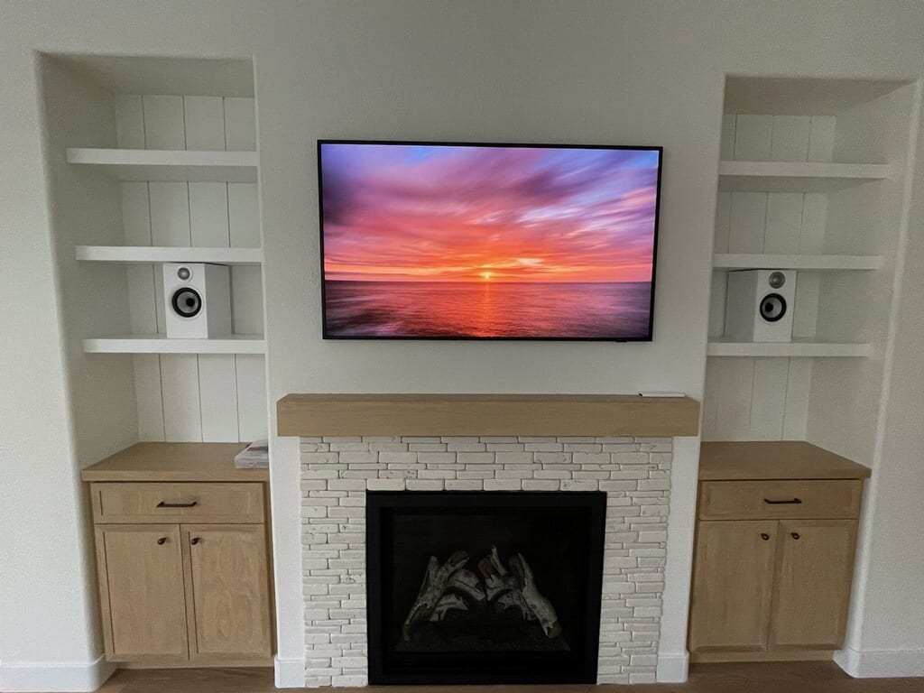 Living room fireplace with white stacked-stone surround, wood mantel, mounted TV, and custom built-in cabinetry and shelving