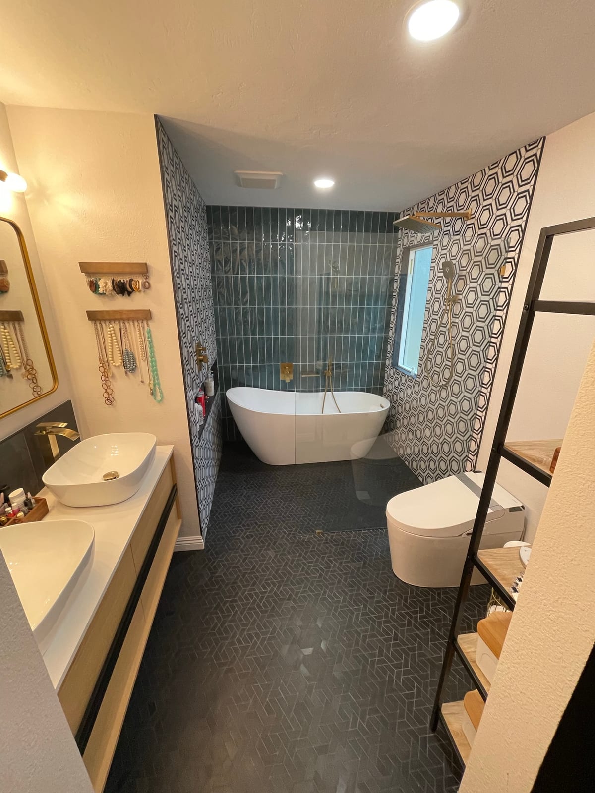 Master bathroom with teal stacked-tile shower, black-and-white hexagon feature wall, freestanding tub, and brass fixtures