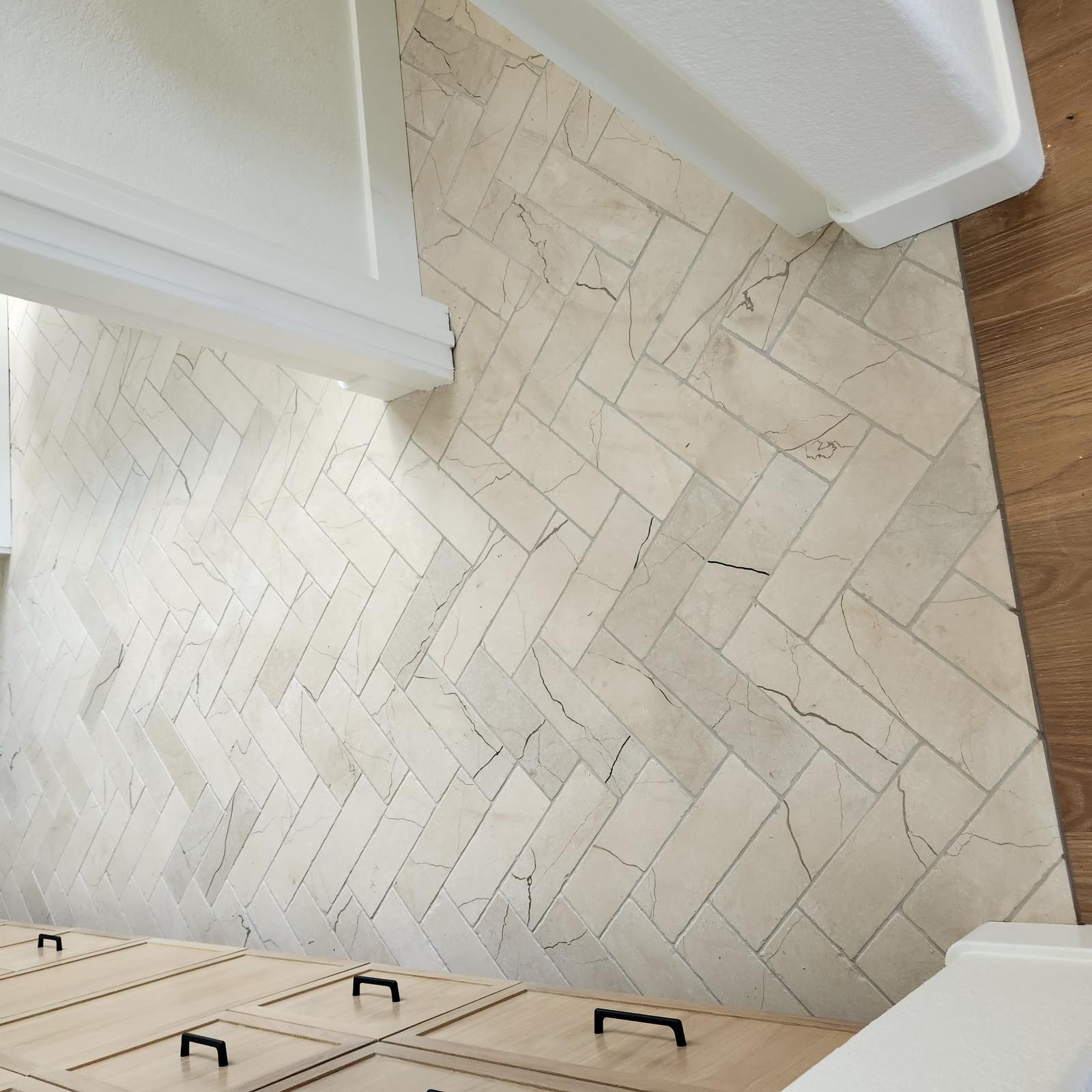 Herringbone marble tile bathroom floor running wall to wall beside a custom wood vanity