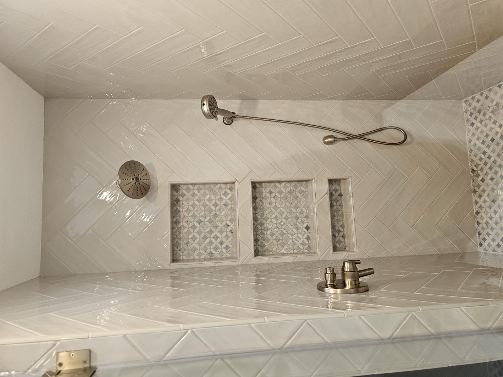 Herringbone tile walk-in shower with three patterned mosaic niches and a mosaic shower pan