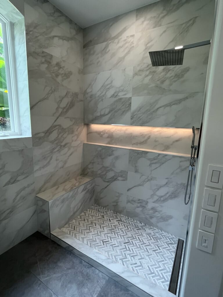 White marble walk-in shower with built-in bench, backlit niche, and herringbone marble floor