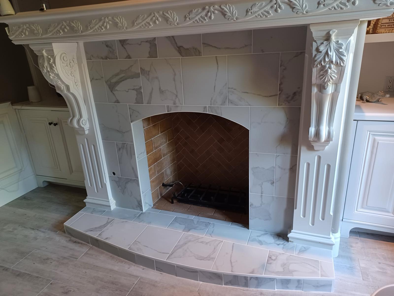 Marble tile fireplace surround and curved raised hearth beneath a carved white mantel
