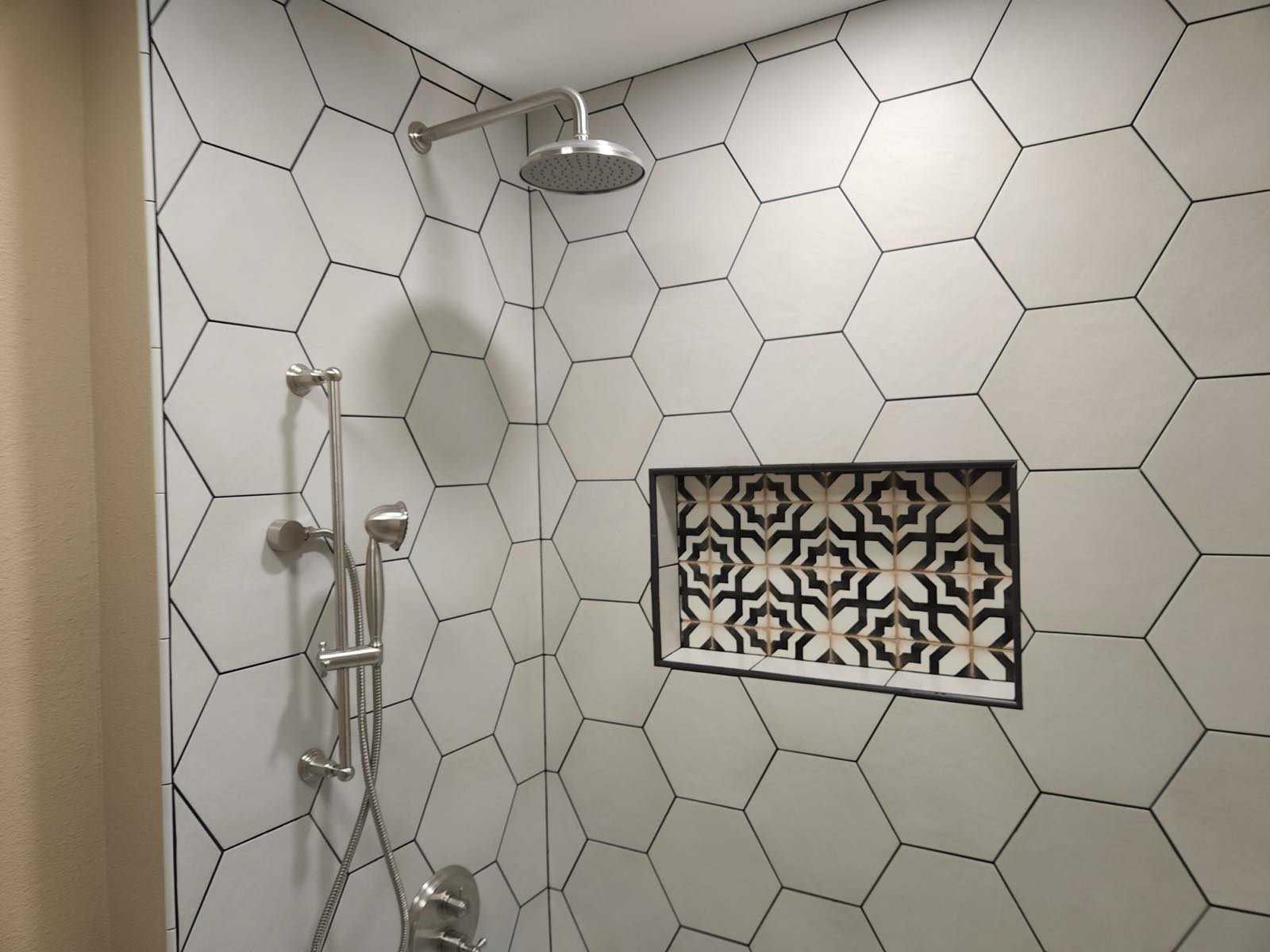 Large white hexagon tile shower wall with a patterned encaustic tile niche and rainfall head